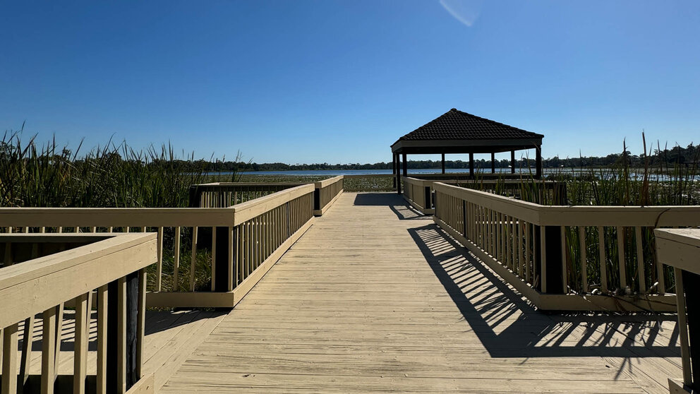 a wooden walkway with a gazebo and a lake