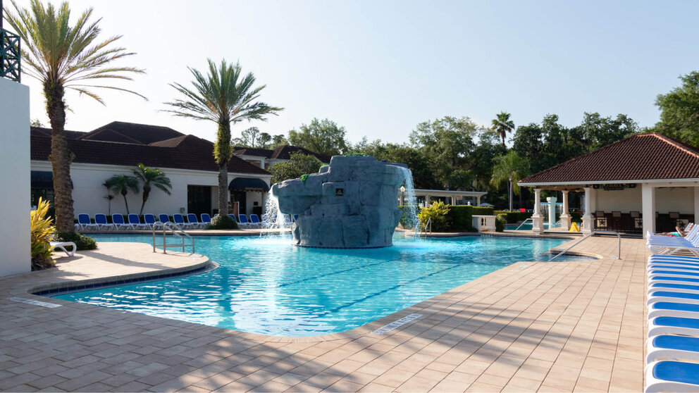 a pool with a rock fountain and a pool with a building and trees