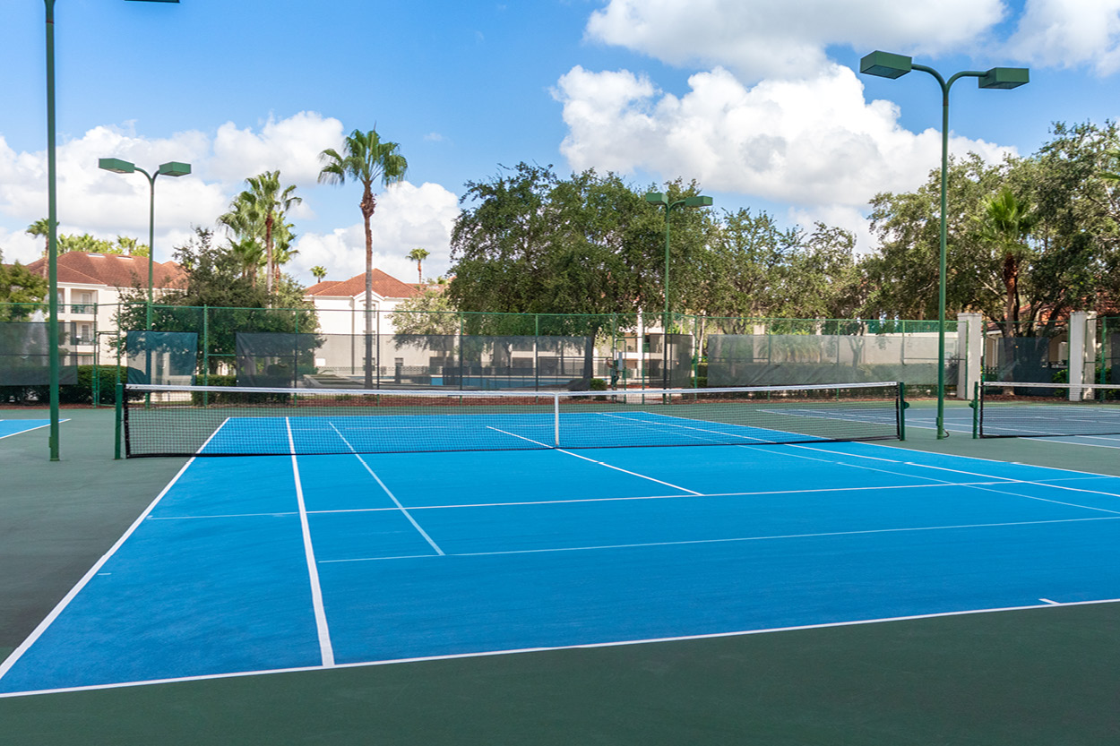 A blue tennis court with a green fence and trees in the background.